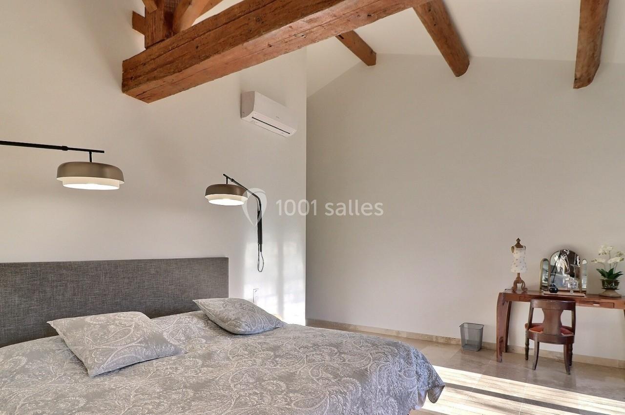 Chambre lumineuse avec lit double, poutres apparentes, bureau en bois et lampes suspendues.