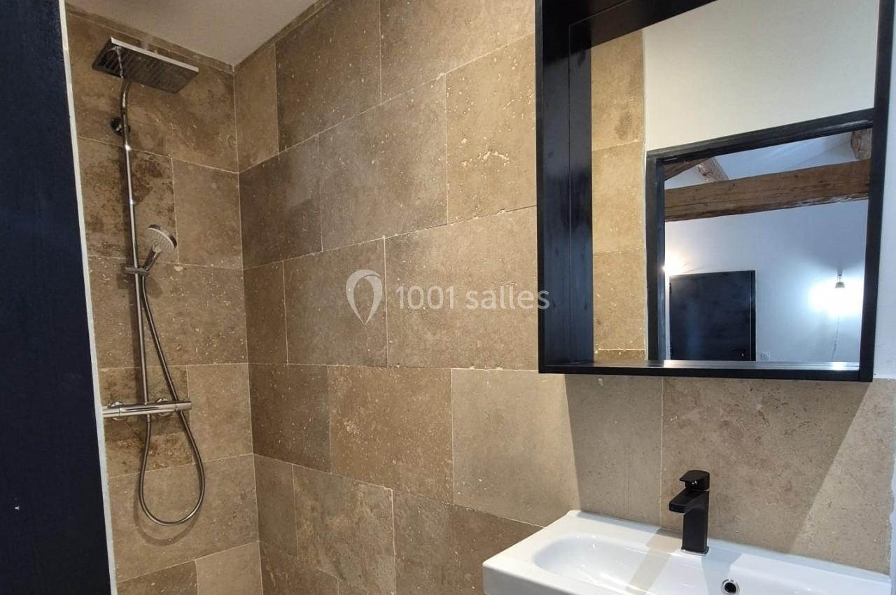 Salle de bain moderne avec douche à l'italienne, carrelage beige, meuble vasque en bois et miroir noir.