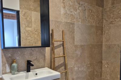 Chambre lumineuse avec lit double, commode en bois, portant à vêtements, télévision et poutre apparente au plafond.