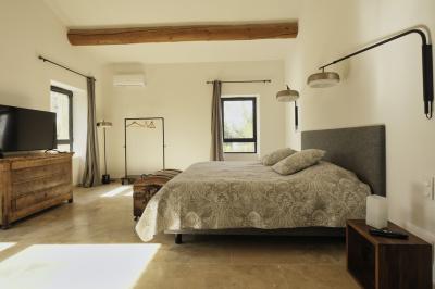 Chambre lumineuse avec lit double, commode en bois, portant à vêtements, télévision et poutre apparente au plafond.