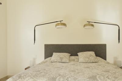 Chambre lumineuse avec lit double, commode en bois, portant à vêtements, télévision et poutre apparente au plafond.