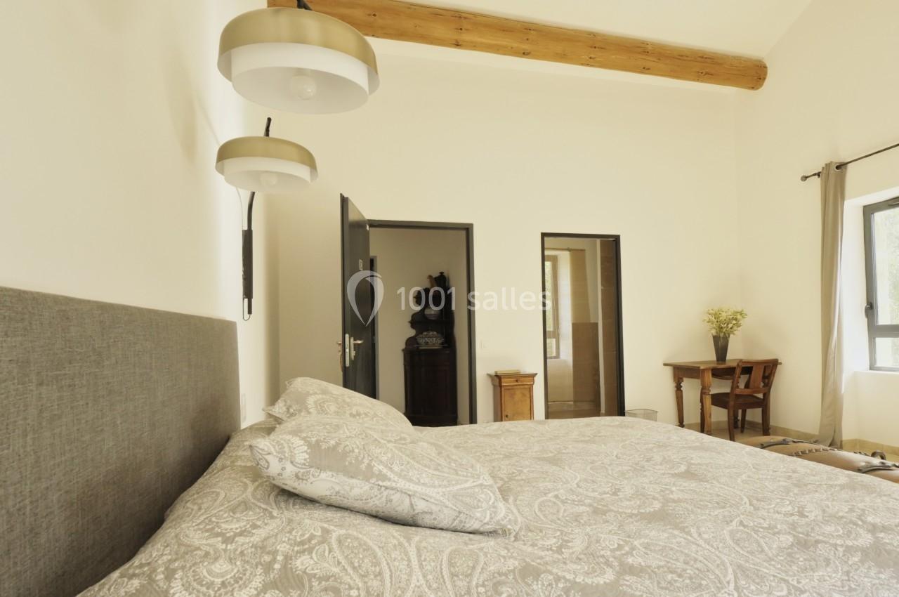 Chambre lumineuse avec lit double, linge à motifs, poutres apparentes, bureau en bois et lampes suspendues.