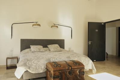 Chambre lumineuse avec lit double, commode en bois, portant à vêtements, télévision et poutre apparente au plafond.