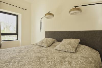 Chambre lumineuse avec lit double, commode en bois, portant à vêtements, télévision et poutre apparente au plafond.