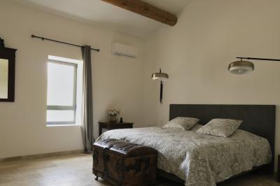 Chambre lumineuse avec lit double, commode en bois, portant à vêtements, télévision et poutre apparente au plafond.