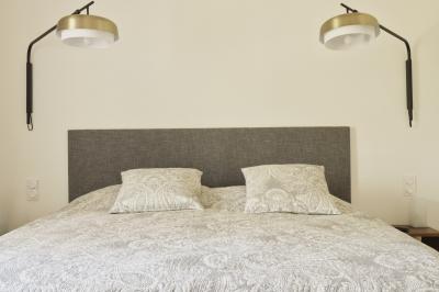Chambre lumineuse avec lit double, commode en bois, portant à vêtements, télévision et poutre apparente au plafond.
