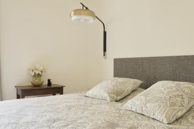 Chambre lumineuse avec lit double, commode en bois, portant à vêtements, télévision et poutre apparente au plafond.