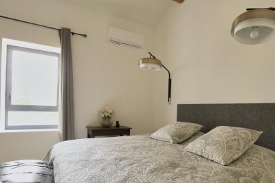 Chambre lumineuse avec lit double, commode en bois, portant à vêtements, télévision et poutre apparente au plafond.