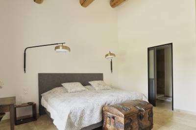 Chambre lumineuse avec lit double, commode en bois, portant à vêtements, télévision et poutre apparente au plafond.