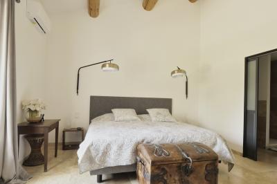Chambre lumineuse avec lit double, commode en bois, portant à vêtements, télévision et poutre apparente au plafond.