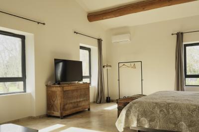 Chambre lumineuse avec lit double, commode en bois, portant à vêtements, télévision et poutre apparente au plafond.