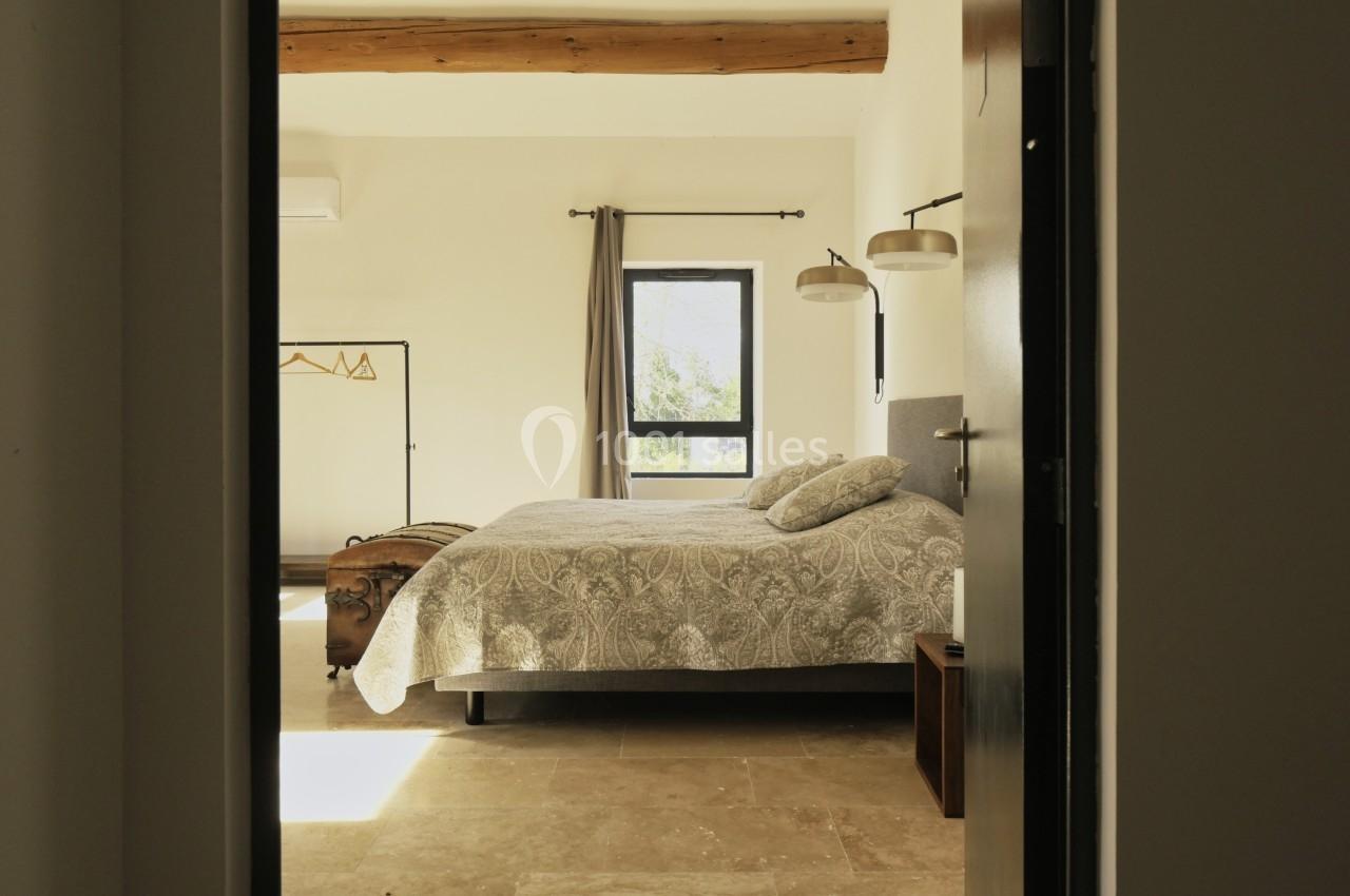 Chambre lumineuse avec lit double, couvre-lit à motifs, poutre apparente, fenêtre donnant sur un paysage verdoyant.