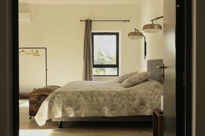 Chambre lumineuse avec lit double, commode en bois, portant à vêtements, télévision et poutre apparente au plafond.