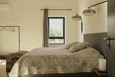 Chambre lumineuse avec lit double, commode en bois, portant à vêtements, télévision et poutre apparente au plafond.