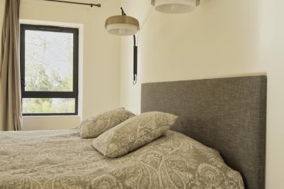 Chambre lumineuse avec lit double, commode en bois, portant à vêtements, télévision et poutre apparente au plafond.