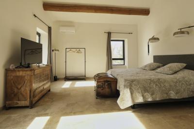 Chambre lumineuse avec lit double, commode en bois, portant à vêtements, télévision et poutre apparente au plafond.