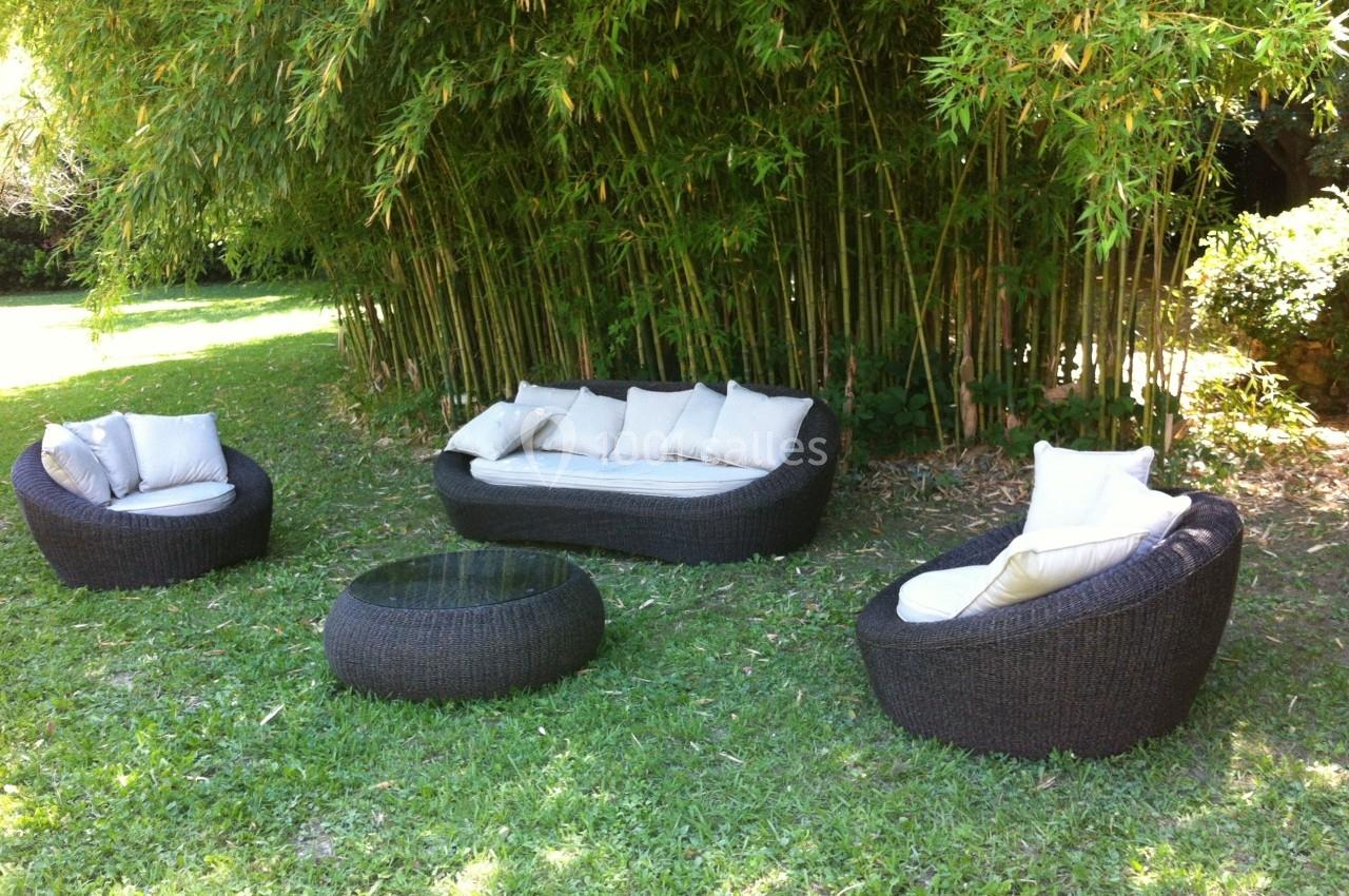 Mobilier de jardin en rotin avec coussins blancs, disposé sur une pelouse devant un bosquet de bambous.