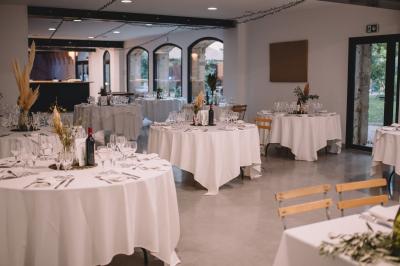 Tables rondes dressées avec nappes blanches et chaises en bois, disposées en extérieur sous des arbres verdoyants.