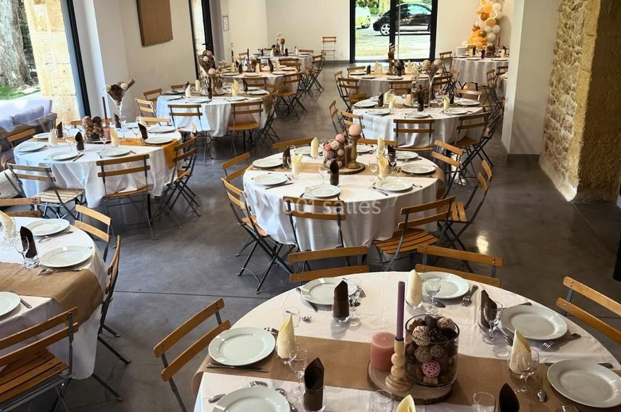 Salle de réception décorée avec des tables rondes dressées, nappes blanches et éléments de décoration champêtres.