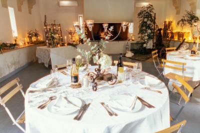 Tables rondes dressées avec nappes blanches et chaises en bois, disposées en extérieur sous des arbres verdoyants.