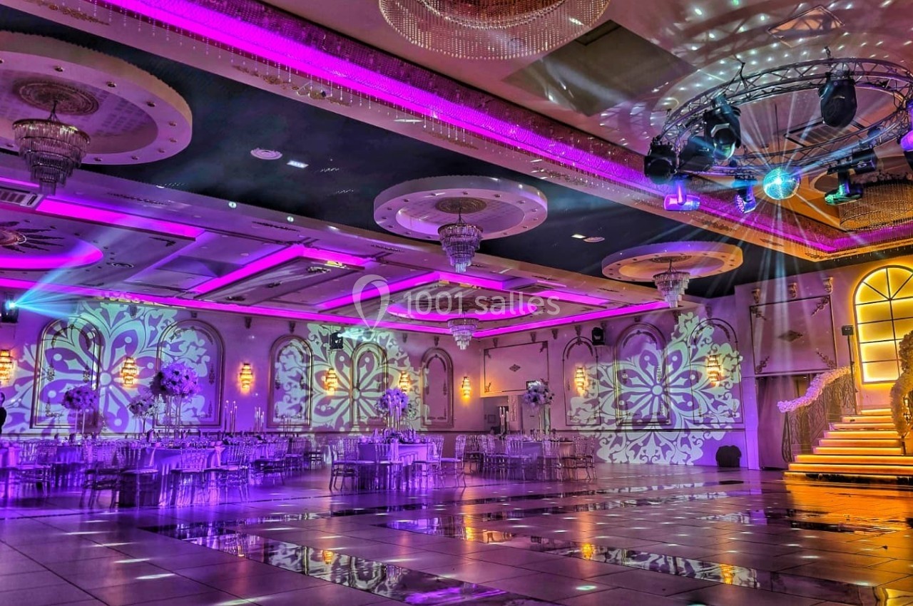 Salle de réception élégante avec éclairage violet, décorations florales et projections lumineuses sur les murs.