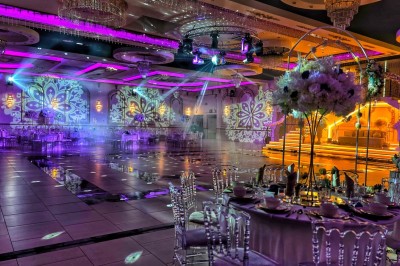 Table ronde élégamment dressée avec nappes blanches, chaises transparentes, centre de table floral et bougies hautes.