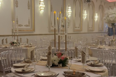 Table ronde élégamment dressée avec nappes blanches, chaises transparentes, centre de table floral et bougies hautes.