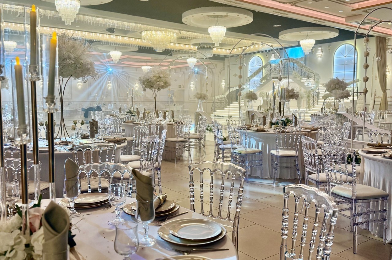 Salle de réception élégante avec tables dressées, chaises transparentes et décorations lumineuses sous des lustres imposants.