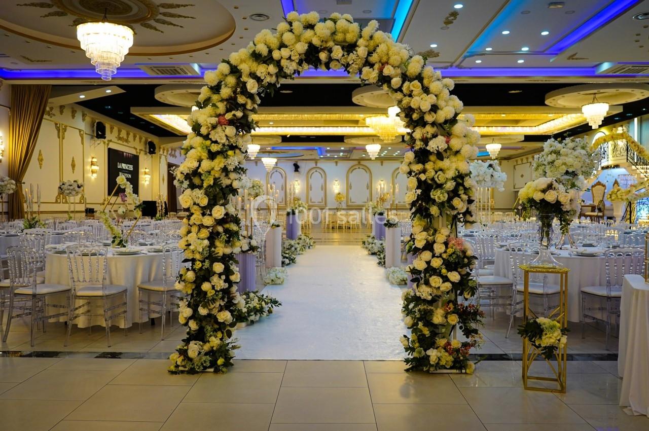 Salle de réception décorée avec des arches fleuries, des tables dressées et un éclairage élégant.
