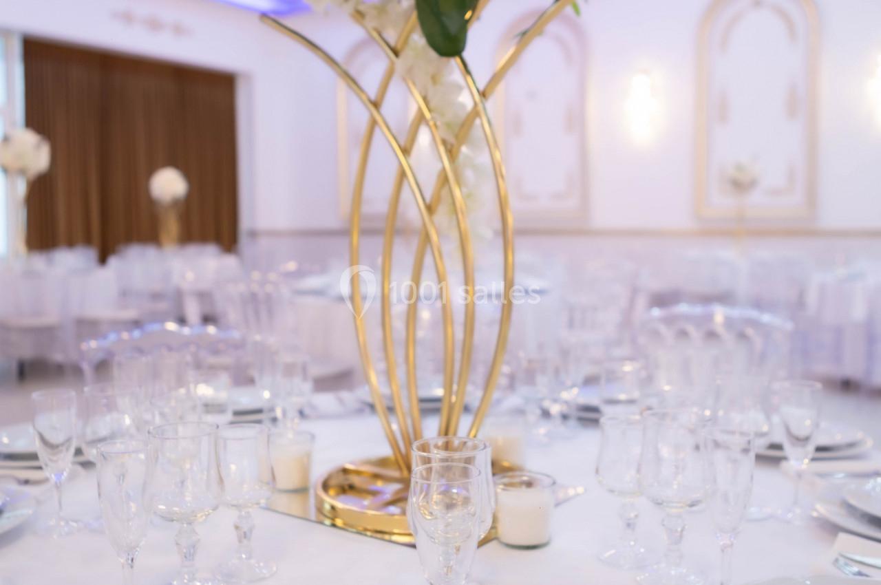 Centre de table floral avec vase doré sur une table dressée dans une salle de réception élégante.