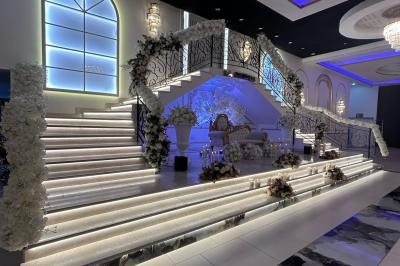 Deux fauteuils dorés ornés de motifs, entourés de fleurs blanches et roses, devant un rideau beige.