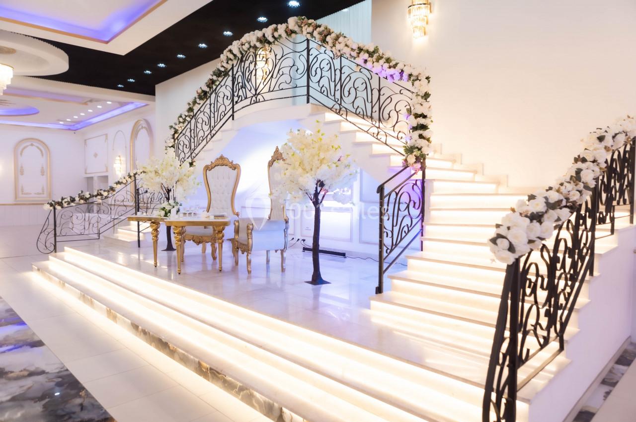 Escalier décoré de fleurs blanches dans une salle lumineuse avec table et chaises élégantes au centre.