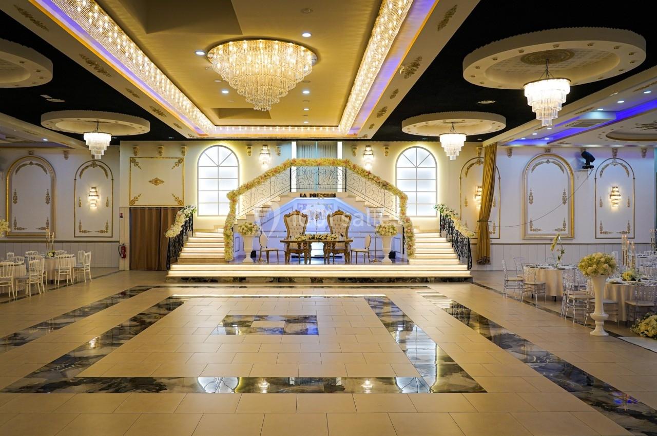 Salle de réception élégante avec escalier central, lustres imposants et décoration florale raffinée.