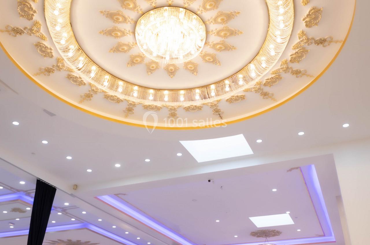 Plafond orné de dorures et d'un grand lustre central dans une salle de réception élégante et lumineuse.