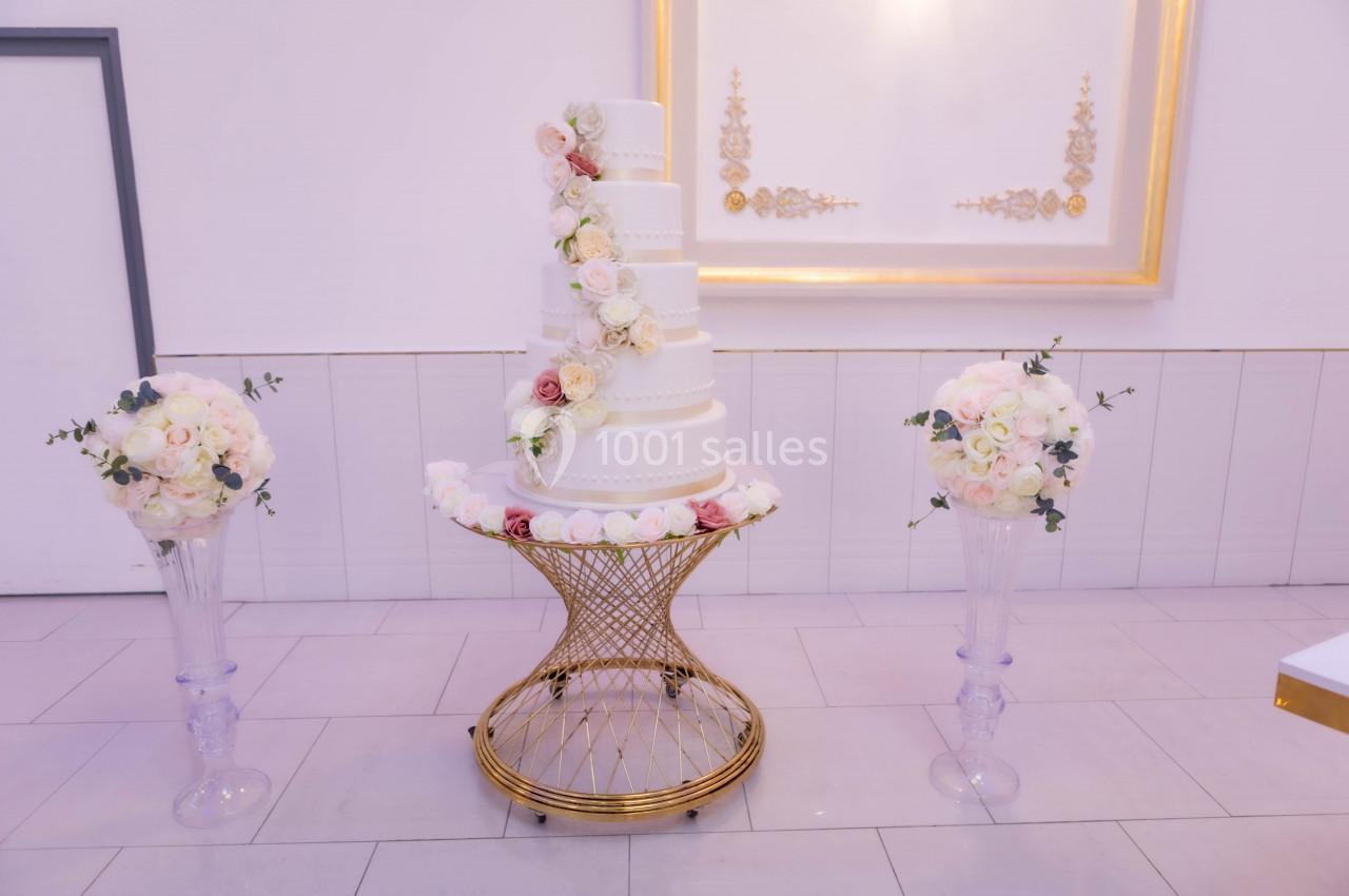 Gâteau de mariage blanc à plusieurs étages décoré de fleurs, entouré de bouquets sur des supports en verre.