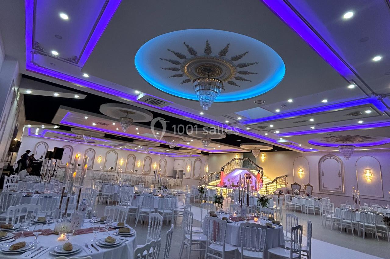 Salle de réception élégante avec tables dressées, éclairage violet et lustres décoratifs au plafond.