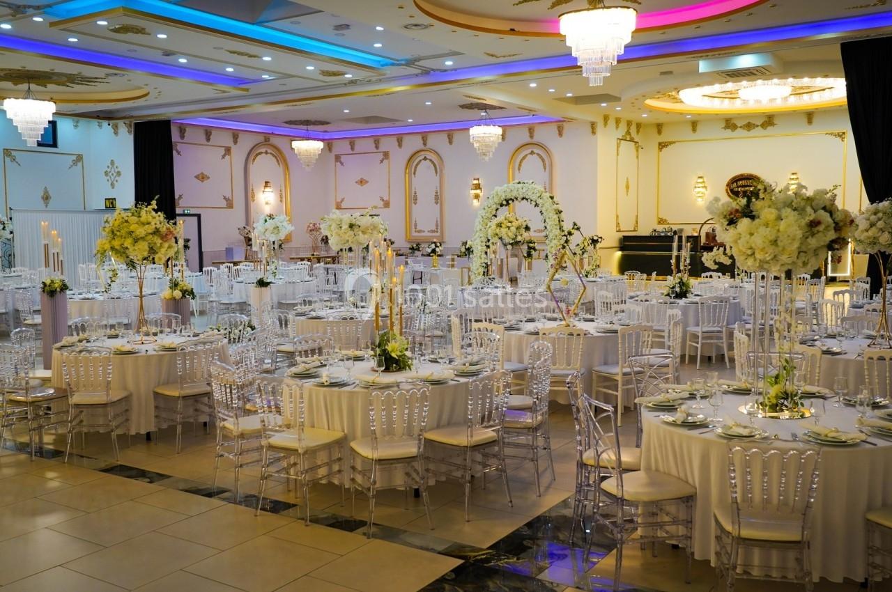 Salle de réception élégante avec tables décorées de nappes blanches, chandeliers et arrangements floraux.