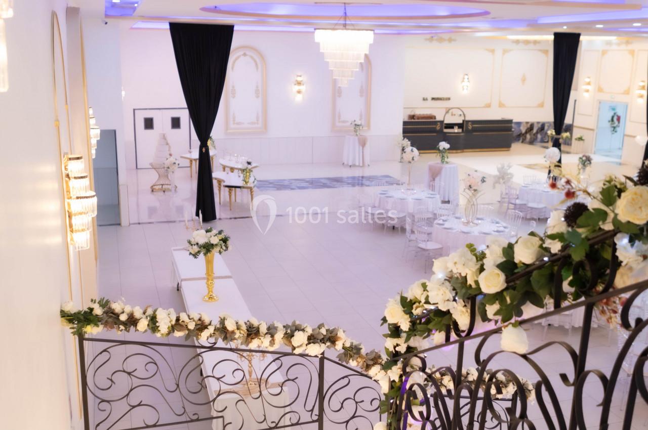 Escalier décoré de fleurs blanches menant à une salle de réception élégante avec tables et lustres.