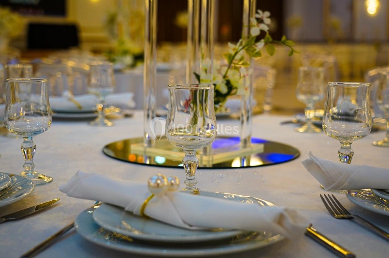 Table élégamment dressée avec assiettes, verres, serviettes roulées et décoration florale sur un miroir central.