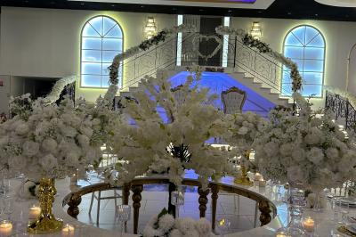 Deux fauteuils dorés ornés de motifs, entourés de fleurs blanches et roses, devant un rideau beige.