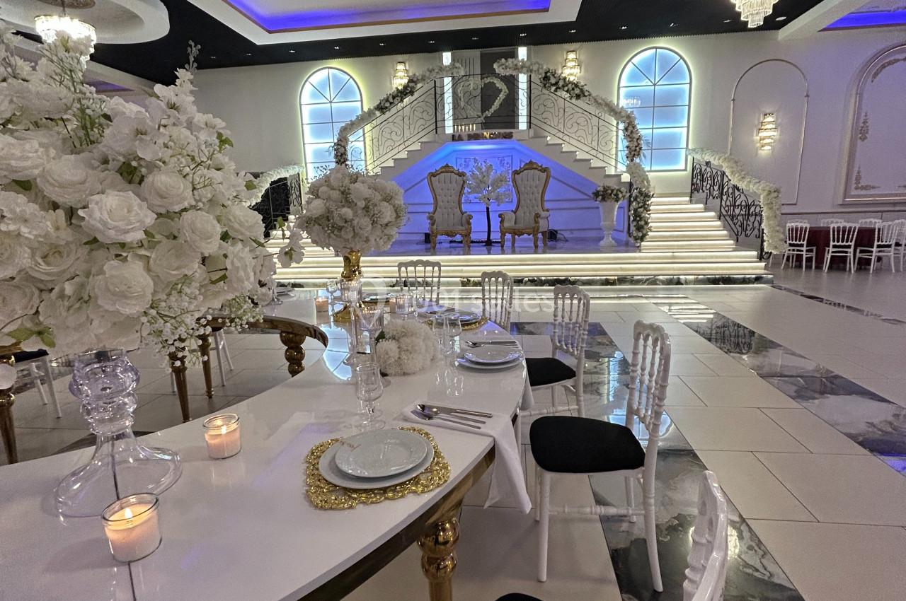 Salle de réception élégante avec table décorée, chandelles, fleurs blanches et escalier central illuminé.