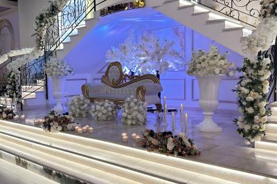 Deux fauteuils dorés ornés de motifs, entourés de fleurs blanches et roses, devant un rideau beige.