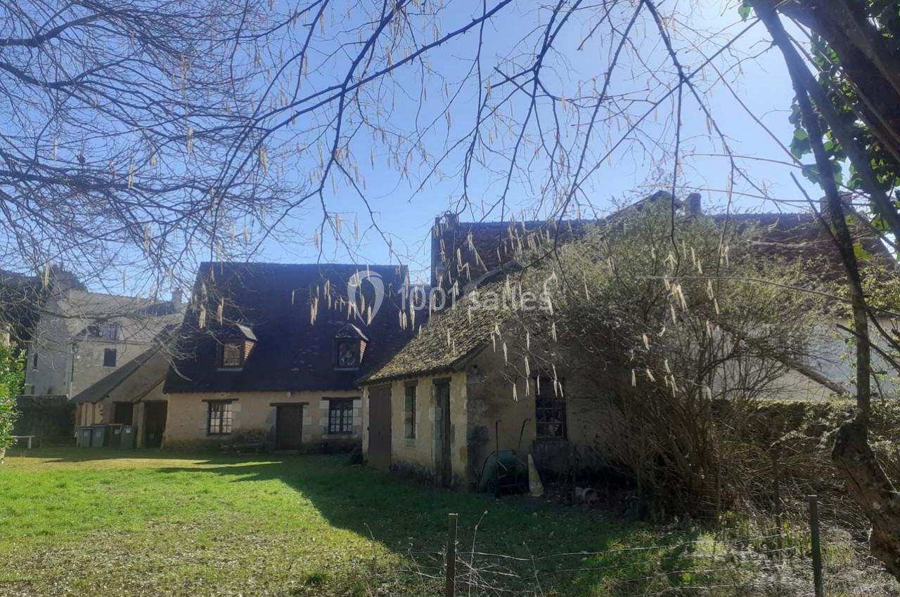Vieilles maisons en pierre avec toits en pente entourées d'arbres et d'un jardin sous un ciel ensoleillé.