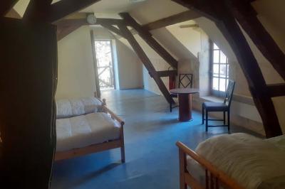 Salle rustique avec tables et chaises en bois, sol en carrelage ancien, poutres apparentes et lumière naturelle.