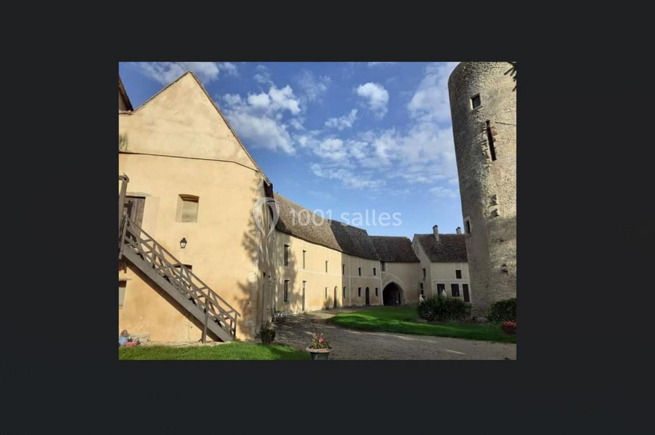 Cour intérieure d'un bâtiment historique avec murs en pierre claire, escalier en bois et tour cylindrique.