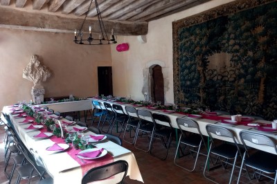 Salle rustique avec tables et chaises en bois, sol en carrelage ancien, poutres apparentes et lumière naturelle.