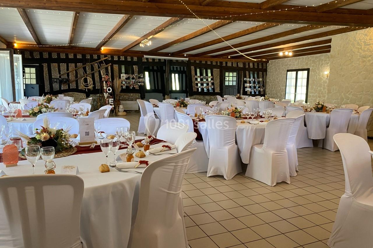 Salle de réception décorée avec des tables rondes, nappes blanches, chaises houssées et arrangements floraux.