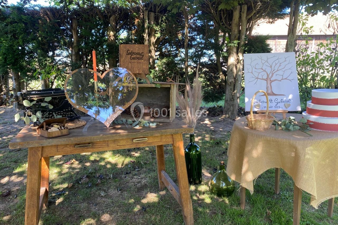 Décoration champêtre avec table en bois, objets rustiques, cœur en verre et arbre à empreintes sous des arbres.