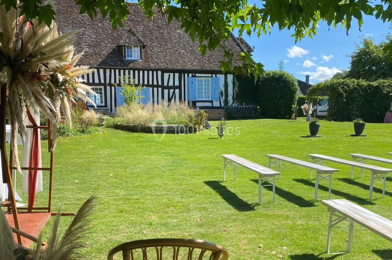 Jardin verdoyant avec bancs blancs disposés devant une maison à colombages sous un ciel bleu.
