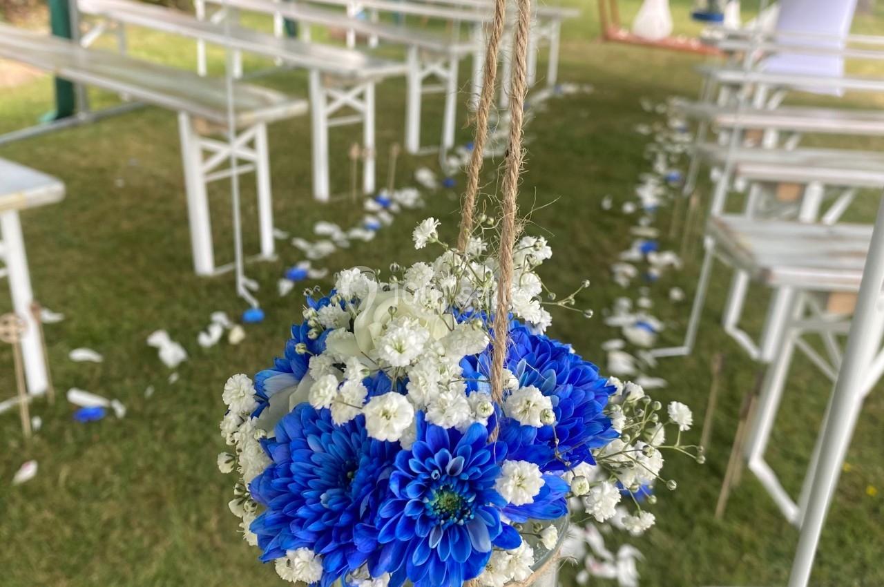 Bouquet de fleurs bleues et blanches suspendu dans un bocal en verre, décorant une allée extérieure pour un événement.